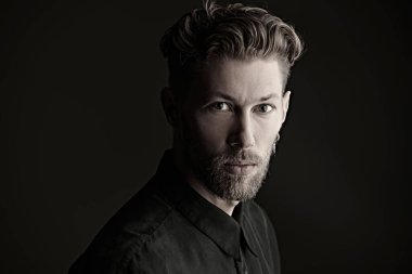 Siyah arka planda sakallı, bıyıklı ve zarif saç stili olan olgun bir adamın portresi. Erkek güzeli. Saç stili.