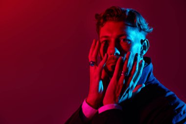 Siyah ceketli, bakımlı, olgun bir adam ellerini yüzünün yanında tutuyor. Erkek güzeli. Burgonya arkaplanı. Karışık renkli ışıklandırma. Boşluğu kopyala.