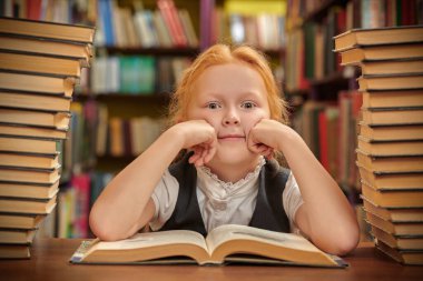 Üniformalı rüya gibi bir kız okul kütüphanesinde sırıtan kitap yığınlarının arasında oturuyor. Modern çocuklar ve eğitim.