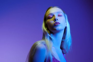 Nazik pembe makyajlı, mavi ve mor arkaplanda gözleri kapalı güzel bir sarışın kız modeli. Güzellik konsepti. Makyaj ve makyaj malzemeleri. Boşluğu kopyala.