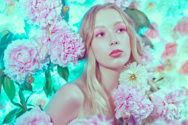 Güzellik ve parfüm konsepti. Dalgalı sarı saçlı, açık pembe makyajlı, narin beyaz ve pembe çiçeklerin arasında ilahi bir kızın portresi. Makyaj ve makyaj malzemeleri. Boşluğu kopyala.