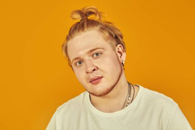 Sıradan giyinmiş tombul bir genç adam kameraya düşünceli bir şekilde bakar. Fotokopi alanı olan sarı bir arkaplanda stüdyo çekimi. Modern gençler..