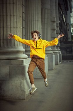 Şehirli bir sokakta sevinçten zıplayıp kulaklıkla müzik dinleyen mutlu bir delikanlı. Yaz, aktif yaşam tarzı. Mutluluk.