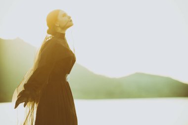 Siyah bir elbise içinde güzel, zarif bir kadın deniz kenarındaki duvağın altında duruyor. Sanki birini bekliyormuş gibi dalgın dalgın uzaklara bakıyor. 19. yüzyıl romanı. 