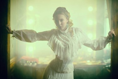 Viktorya tarzı. 19. yüzyıl tarzında, kadınsı beyaz bir elbise giymiş sevimli genç bir bayan klasik bir odada duruyor. Vintage iç mimari.