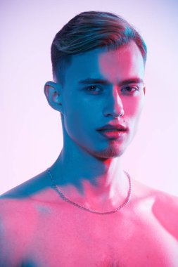 Stüdyoda, çok renkli ışıkta arka planda çıplak duran çekici ve atletik gövdeli genç bir adamın çekimleri. Erkeklerin güzelliği ve sağlığı. 