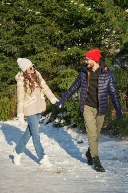 Neşeli genç çift güneşli bir günde kış parkında yürüyüş yapıyor. Kış günün kutlu olsun. Kış aktiviteleri. Moda..