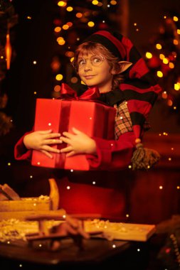 Noel Masalı. Küçük sevimli elf çocuk tahta oyuncakları hediye kutularına koyar. Noel Baba atölyesi. Sihirli ışıklar yanıp sönüyor.