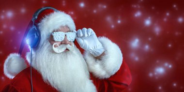 Noel ve yeni yıl kutlaması. Neşeli disko Noel Baba 'nın, kulaklıklı ve karlı güneş gözlüklü portresi. Parıltılı kırmızı arkaplan, neşeli ışıklar ve kopyalama alanı. 