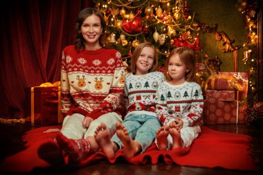 Güzel anne ve sevgili kızları Noel arifesinde Noel arifesini rahat bir aile ortamında Noel ağacının yanında oturarak geçiriyorlar. Mutlu Noeller. Tam boy çekim. 