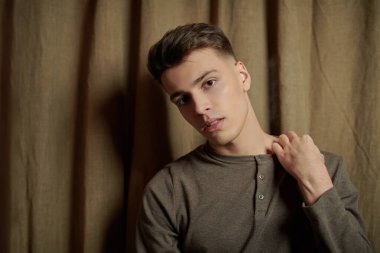 Gri kazaklı yakışıklı bir gencin portresi kahverengi perde arkasında. Gençlik modası. Erkek güzeli, saç stili. Stüdyo resmi.