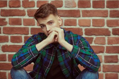 Kotlu yakışıklı sakin bir genç adam ve tuğla bir duvara karşı flanel bir gömlek. Gençlik modası. İnsanlar ve duygular. Stüdyo resmi.