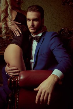 Handsome man in evening clothes hugs his sexy beloved girl for the ass in a luxury vintage apartment. Passionate love.