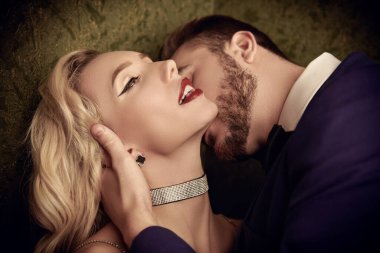 Güzel bir çift sarışın kadın ve esmer adam lüks bir odada öpüşüyor. Aşk ve tutku. Akşam güzelliği ve moda.