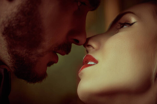 Close-up portrait of a beautiful couple of an adorable blond woman and brunet man is kissing each other. Love and passion. Evening beauty and fashion.