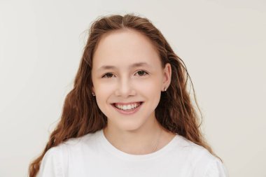 Mutlu çocuk konsepti. Kameraya gülümseyen uzun dalgalı saçlı güzel bir genç kızın portresi. Beyaz stüdyo geçmişi.