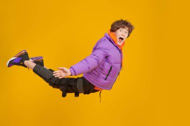 Havada havalı parlak elbiseler ve kulaklıklar takan genç bir çocuk uçuyor. Modern gençlerin yaşam tarzı. Kopyalama alanı olan sarı arkaplan. 