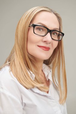 Klasik beyaz bluz ve gözlüklü, orta yaşlı, mutlu bir iş kadınının fotoğrafı. Gri stüdyo geçmişi. Gözlük stili. 