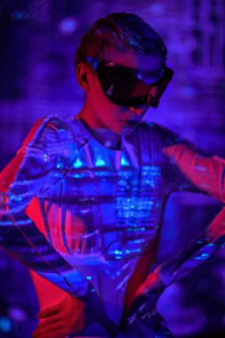 Sanal oyunlar. Fütürist aynalı gözlüklü ve tulumlu mükemmel siber punk kızı kırmızı ışık ve ateş yansımaları içinde duruyor. Geleceğin siber dünyası.