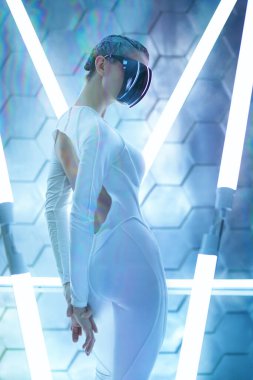 Gelecekteki siber dünyanın konsepti. VR oyunları. Beyaz önlüklü ve aynalı maske gözlüklü fütürist bir kız neon lambaların arasında duruyor.. 