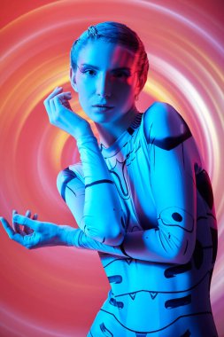 Fütürist teknoloji tulumlu mükemmel siber punk kızı mavi ışıkta ve kırmızı arka planda kırmızı daireler çizerek duruyor. Geleceğin siber dünyası. Sanal oyunlar.