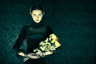 Gotik roman, mistisizm. Zarif siyah kadife elbiseli dramatik bir esmer kız gecenin karanlığında elinde bir buket solmuş gülle arka planda duruyor. Boşluğu kopyala.