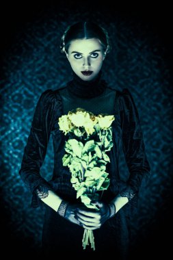 Gotik roman, mistisizm. Zarif siyah kadife elbiseli dramatik bir esmer kız gecenin karanlığında elinde bir buket solmuş gülle eski bir arka planda duruyor..