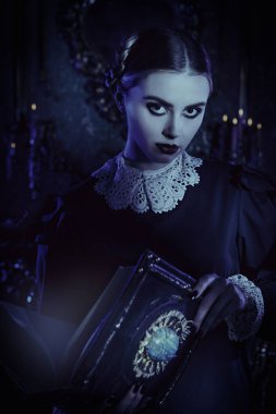 Addams Ailesi romanı. Beyaz yakalı, düzgün siyah elbiseli esmer bir kız gecenin karanlığında kasvetli gotik bir kalede duruyor ve antik bir kitap okuyor. Mistik roman, gotik.