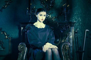 Mistik gotik roman, korku. Kasvetli bir kalede, koltukta oturan, katı siyah elbiseli, beyaz yakalı, tuhaf, esmer bir kızın portresi. Addams Aile Stili. 