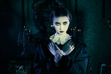 Seçkin siyah kadife elbise ve dantel eldiven giymiş esmer bir kızın gece vakti koyu renkli bir arka planda duruşu. Gotik roman, mistisizm. Makyaj ve saç stili.