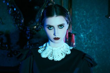 Beyaz yakalı, düzgün siyah elbiseli esmer bir kız kasvetli gotik bir kalede duruyor ve kameraya pek dostça görünmüyor. Addams Ailesi. Gotik kara komedi. Boşluğu kopyala.