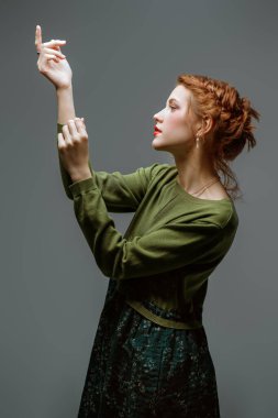 Gri bir stüdyo arka planında zeytin rengi bir elbise içinde narin makyajlı ve kıvırcık saçlı sevimli kızıl saçlı manken kız. Moda ve güzellik portresi. Makyaj ve makyaj malzemeleri, saç stili..