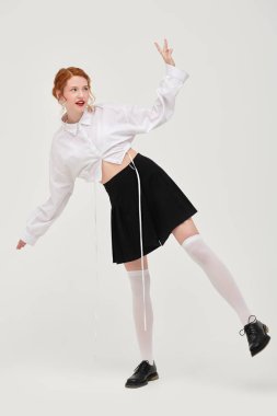 Beyaz gömlekli ve siyah etekli beyaz bir duvara karşı poz veren kızıl saçlı güzel bir kızın tam boy portresi. Kadınsı bir tarz. Bahar ve yaz modası. 