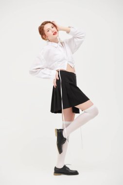 Beyaz gömlekli ve siyah etekli beyaz bir duvara karşı poz veren kızıl saçlı güzel bir kızın tam boy portresi. Kadınsı bir tarz. Bahar ve yaz modası. 