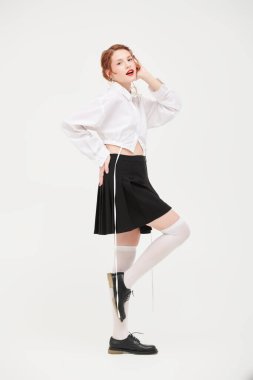 Bahar ve yaz modası. Beyaz gömlekli ve siyah etekli beyaz bir duvara karşı poz veren kızıl saçlı güzel bir kızın tam boy portresi. Kadınsı bir tarz.. 