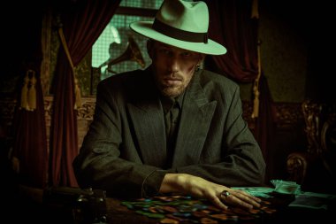 Mafyanın suç dünyasına. Zarif siyah takım elbiseli ve beyaz şapkalı sert bir gangster lüks bir dairede oturuyor ve kart oynuyor. Retro tarzı. Dedektif filmi.