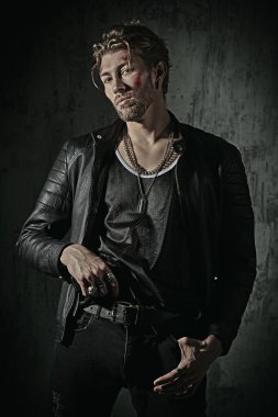 Kötü adam konsepti. Yüzünde morluklar ve yaralar olan, beton duvarlı karanlık bir odada elinde silahla duran sert bir erkek haydut vuruldu. Aksiyon filmi kahramanı.