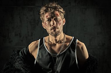 Kötü adam konsepti. Yüzünde morluklar ve yaralar olan, beton duvarlarla karanlık bir odada duran ve kameraya güvenle bakan sert bir erkek haydudun portresi. Aksiyon filmi kahramanı.
