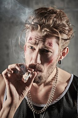 Kötü adam konsepti. Yüzünde morluklar ve yaralar olan, beton duvarlarla karanlık bir odada sigara içen sert bir erkek haydudun portresi. Aksiyon filmi kahramanı.