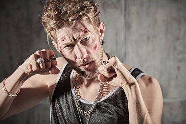 Yüzünde morluklar ve yaralar olan, beton duvarlarla karanlık bir odada duran ve saldırganca bakan sert bir erkek haydudun fotoğrafı. Kötü adam konsepti. Aksiyon filmi kahramanı.