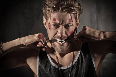 Yüzünde çizikler ve yaralar olan, beton duvarların önünde kameraya bakan vahşi bir adamın portresi. Aksiyon filmi kahramanı. Dedektif filmi. Kötü adam..