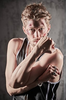 Yüzünde çizikler ve yaralar olan, beton duvarların önünde kameraya bakan vahşi bir adamın portresi. Aksiyon filmi kahramanı. Dedektif filmi. Kötü adam..