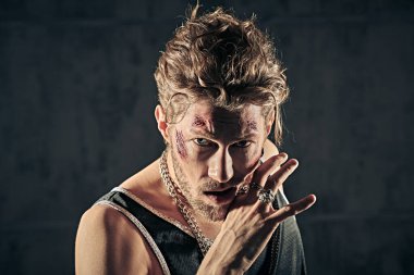 Yüzünde morluklar ve yaralar olan, beton duvarlarla karanlık bir odada duran ve saldırganca bakan sert bir erkek haydudun portresi. Kötü adam konsepti. Aksiyon filmi kahramanı. 