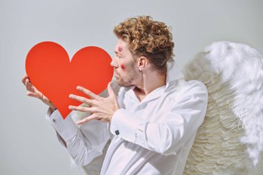 Aşk için savaş. Cesur yakışıklı adam aşk tanrısı yüzünde yaralar olan aşk tanrısı ellerinde kırmızı bir kalp tutuyor. Sevgililer Günü.