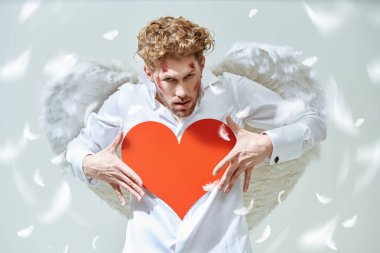 Aşk için savaş. Cesur yakışıklı adam aşk tanrısı yüzünde yaralar olan aşk tanrısı ellerinde kırmızı bir kalp tutuyor. Sevgililer Günü.