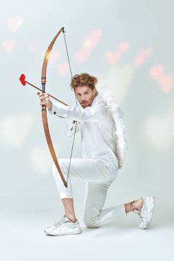 Cesur aşk tanrısı Cupid 'in tam boy portresi, kurbanına bir ok atmak niyetinde. Fantezi. Stüdyo beyaz arka plan. Aşk konsepti. Sevgililer Günü.