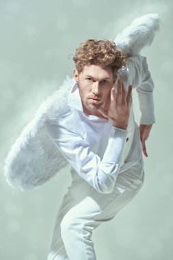 Beyaz gömlekli ve beyaz kanatlı hızlı yakışıklı bir erkek melek öne doğru koşar. Beyaz stüdyo geçmişi. Sevgililer Günü. Fantezi kahramanı.