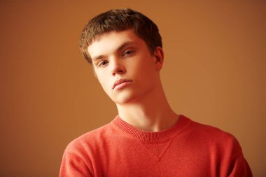 Modern bir gencin portresi sakince ve düşünceli görünüyor. Fotokopi alanı olan kahverengi bir stüdyo. Parlak renkler.