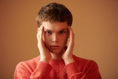 Düşünceli görünen modern bir gencin portresi. Fotokopi alanı olan kahverengi bir stüdyo. Parlak renkler.