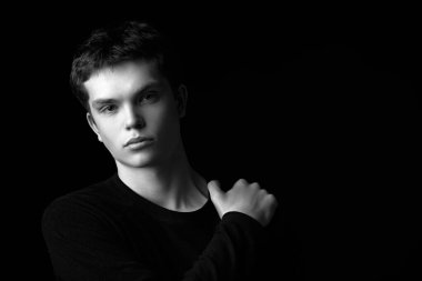 Siyah kazaklı düşünceli bir gencin siyah beyaz portresi sakince kameraya bakıyor. Psikoloji, iç dünya. Kopyalama alanı olan siyah arkaplan.